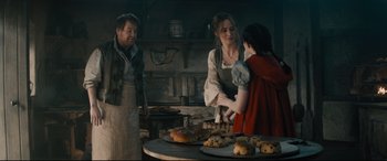 Movie still from “Into the Woods” (2014), directed by Rob Marshall – Two women and a man standing in front of a table with food on top of it; Medium shot, Over the shoulder angle