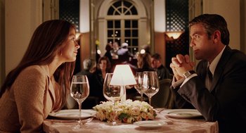Movie still from “Intolerable Cruelty” (2003), directed by Joel Coen – Two people sitting at a dinner table with wine glasses; Medium shot, Over the shoulder angle