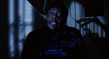 Movie still from “Intolerable Cruelty” (2003), directed by Joel Coen – A man with a beard is sitting in a dark room; Close Up shot, Low angle