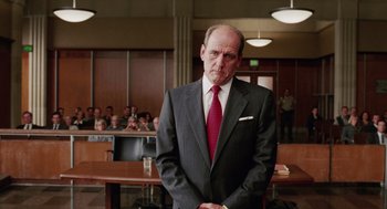 Movie still from “Intolerable Cruelty” (2003), directed by Joel Coen – A man in a suit and tie standing in front of a group of people; Medium shot, Low angle