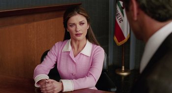 Movie still from “Intolerable Cruelty” (2003), directed by Joel Coen – A woman sitting at a desk in front of an american flag; Medium shot, Over the shoulder angle