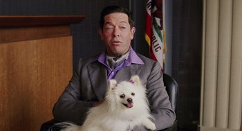 Movie still from “Intolerable Cruelty” (2003), directed by Joel Coen – A man sitting in a chair holding a white dog; Medium shot, Over the shoulder angle