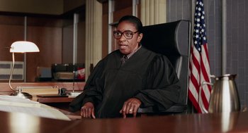Movie still from “Intolerable Cruelty” (2003), directed by Joel Coen – A judge sitting at a table in a courtroom; Medium shot, Low angle