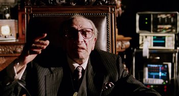 Movie still from “Intolerable Cruelty” (2003), directed by Joel Coen – An old man wearing a suit and tie sitting in a chair; Close Up shot, Over the shoulder angle