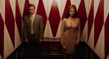 Movie still from “Intolerable Cruelty” (2003), directed by Joel Coen – A man and a woman standing next to each other in front of a wall; Medium shot, Low angle