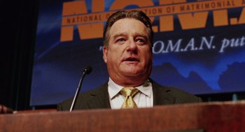 Movie still from “Intolerable Cruelty” (2003), directed by Joel Coen – A person at a podium with a microphone; Close Up shot, Low angle