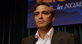 Movie still from “Intolerable Cruelty” (2003), directed by Joel Coen – A man in a suit and tie standing in front of a microphone; Close Up shot, Low angle
