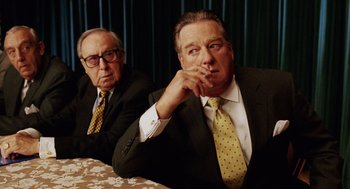 Movie still from “Intolerable Cruelty” (2003), directed by Joel Coen – Two men sitting at a table in suits and ties; Medium shot, Over the shoulder angle