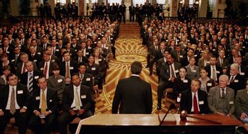 Movie still from “Intolerable Cruelty” (2003), directed by Joel Coen – A group of men in suits sitting in front of a podium; Extreme Wide shot, High angle