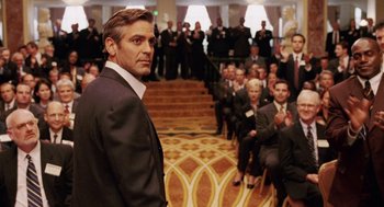 Movie still from “Intolerable Cruelty” (2003), directed by Joel Coen – A man in a suit standing in front of a group of people; Medium shot, Over the shoulder angle