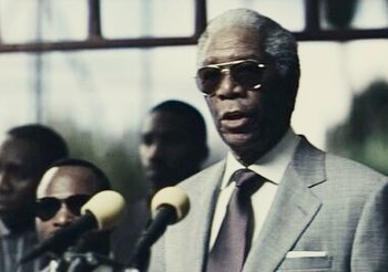 Movie still from “Invictus” (2009), directed by Clint Eastwood – An older man wearing a suit and sunglasses; Close Up shot, Over the shoulder angle