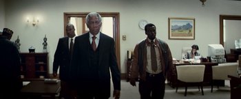 Movie still from “Invictus” (2009), directed by Clint Eastwood – A man in a suit and tie walking down a hall way; Medium shot, Low angle