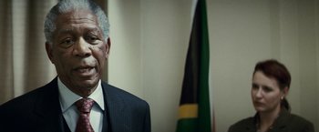 Movie still from “Invictus” (2009), directed by Clint Eastwood – An older man wearing a suit and tie in front of a flag; Close Up shot, Low angle