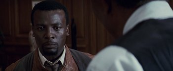 Movie still from “Invictus” (2009), directed by Clint Eastwood – A black man wearing a brown leather jacket and a tie; Close Up shot, Over the shoulder angle