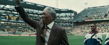 Movie still from “Invictus” (2009), directed by Clint Eastwood – An older man wearing a suit and tie in a stadium; Medium shot, Low angle