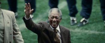 Movie still from “Invictus” (2009), directed by Clint Eastwood – An older man wearing a suit and tie waving; Close Up shot, Low angle