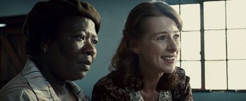 Movie still from “Invictus” (2009), directed by Clint Eastwood – Two women are standing next to each other smiling; Close Up shot, Over the shoulder angle