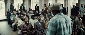 Movie still from “Invictus” (2009), directed by Clint Eastwood – A group of people sitting in front of a man in a suit; Wide shot, High angle