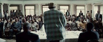 Movie still from “Invictus” (2009), directed by Clint Eastwood – A man standing in front of a group of people; Medium shot, Over the shoulder angle