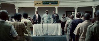 Movie still from “Invictus” (2009), directed by Clint Eastwood – A group of men standing at a podium with microphones; Wide shot, Low angle