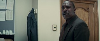 Movie still from “Invictus” (2009), directed by Clint Eastwood – A man in a suit and tie standing in front of a wall; Close Up shot, Low angle