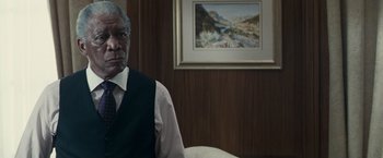 Movie still from “Invictus” (2009), directed by Clint Eastwood – A man in a vest and tie sitting in front of a painting; Close Up shot, Over the shoulder angle