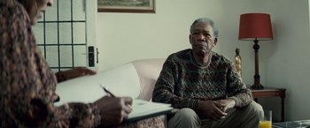 Movie still from “Invictus” (2009), directed by Clint Eastwood – An older man sitting in front of another man; Medium shot, Over the shoulder angle