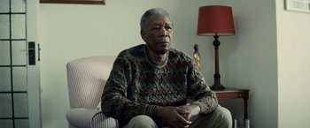 Movie still from “Invictus” (2009), directed by Clint Eastwood – An older man sitting on a couch in a living room; Medium shot, Low angle
