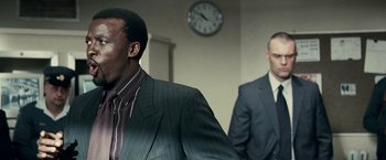 Movie still from “Invictus” (2009), directed by Clint Eastwood – A man in a suit standing next to another man in a suit in front of a wall clock; Close Up shot, Over the shoulder angle