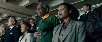 Movie still from “Invictus” (2009), directed by Clint Eastwood – A man and a woman standing next to each other in front of another man; Medium shot, Low angle