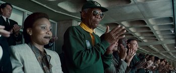 Movie still from “Invictus” (2009), directed by Clint Eastwood – An older man wearing a green and yellow baseball uniform clapping his hands; Medium shot, Low angle