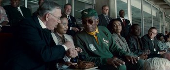 Movie still from “Invictus” (2009), directed by Clint Eastwood – An older man in a green jacket is sitting in front of a group of people; Medium shot, Over the shoulder angle