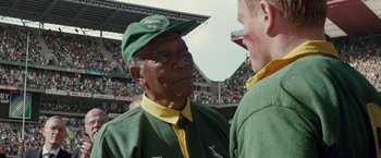 Movie still from “Invictus” (2009), directed by Clint Eastwood – A man wearing a green and yellow hat and a green jacket; Close Up shot, Over the shoulder angle