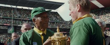 Movie still from “Invictus” (2009), directed by Clint Eastwood – A man in a green and yellow jacket holding a trophy; Close Up shot, Low angle