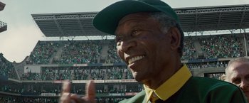 Movie still from “Invictus” (2009), directed by Clint Eastwood – An older man wearing a baseball cap and smiling; Close Up shot, Low angle