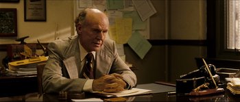 Movie still from “Invincible” (2006), directed by Ericson Core – An older man sitting at a desk with papers; Medium shot, Over the shoulder angle