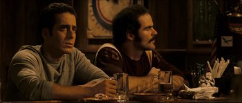 Movie still from “Invincible” (2006), directed by Ericson Core – Two men sitting at a table with drinks in front of them; Medium shot, Over the shoulder angle