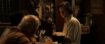 Movie still from “Invincible” (2006), directed by Ericson Core – A man sitting at a table with a bunch of paper in front of him; Medium shot, Over the shoulder angle