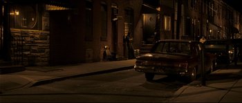 Movie still from “Invincible” (2006), directed by Ericson Core – A man standing on the side of the street at night next to a car; Wide shot, High angle