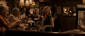 Movie still from “Invincible” (2006), directed by Ericson Core – A woman standing at a bar smiling for the camera; Medium shot, Over the shoulder angle