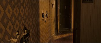Movie still from “Invincible” (2006), directed by Ericson Core – A room that has a door open and a wall that has a hole in it; Wide shot, High angle
