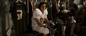 Movie still from “Invincible” (2006), directed by Ericson Core – A man sitting on top of a bench holding a football helmet; Medium shot, Low angle