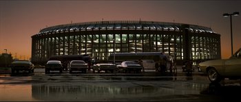 Movie still from “Invincible” (2006), directed by Ericson Core – Cars are parked in a parking lot near a stadium at night; Extreme Wide shot, Low angle