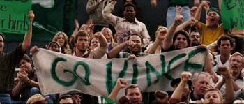 Movie still from “Invincible” (2006), directed by Ericson Core – A group of people that are sitting in front of a banner; Medium shot, High angle