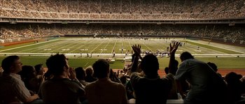 Movie still from “Invincible” (2006), directed by Ericson Core – A group of people sitting in a stadium with their hands raised; Extreme Wide shot, High angle