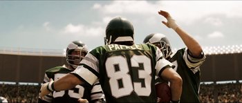 Movie still from “Invincible” (2006), directed by Ericson Core – A group of football players huddle together in a huddle; Medium shot, Over the shoulder angle