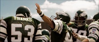 Movie still from “Invincible” (2006), directed by Ericson Core – A group of football players standing next to each other on a field; Medium shot, Over the shoulder angle
