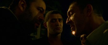 Movie still from “Irreversible” (2002), directed by Gaspar Noé – A group of men standing next to each other in the dark; Close Up shot, Over the shoulder angle