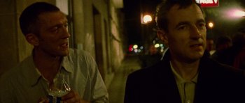 Movie still from “Irreversible” (2002), directed by Gaspar Noé – A man standing next to another man on a sidewalk; Close Up shot, Over the shoulder angle