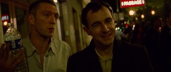 Movie still from “Irreversible” (2002), directed by Gaspar Noé – A man standing next to another man on a sidewalk; Close Up shot, Low angle